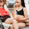 Child eating snacks out of a Govino shatterproof beer can glass outside by the pool while her mother is holding a Govino shatterproof wine glass filled with red wine